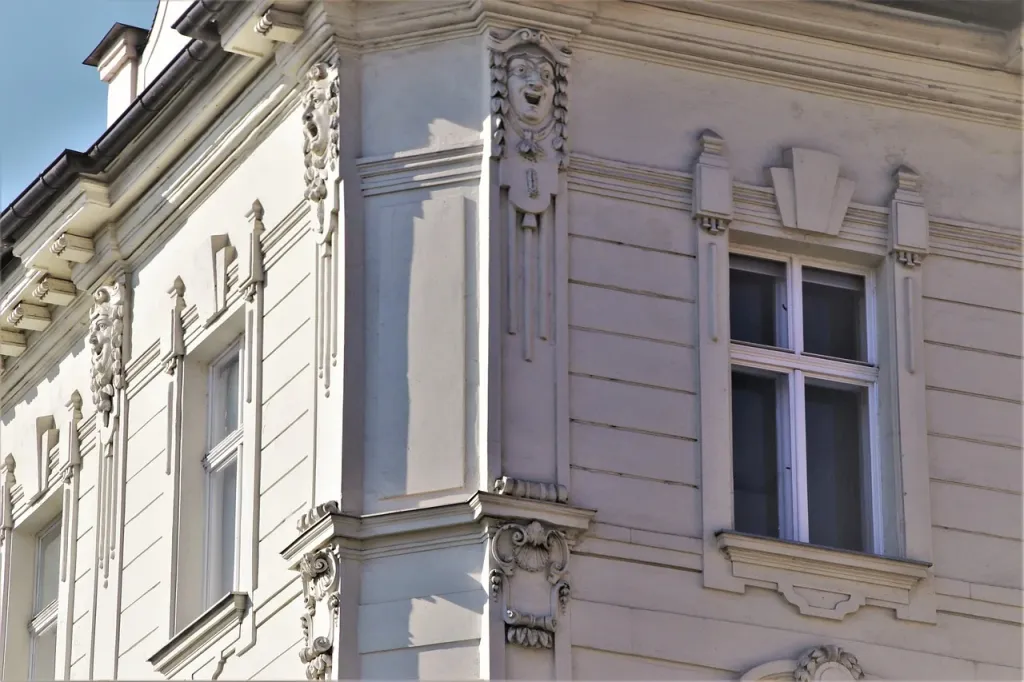 Świeżo nałożony tynk silikonowy o ziarnistej strukturze z widoczną kielnią na tle placu budowy w porannym świetle.